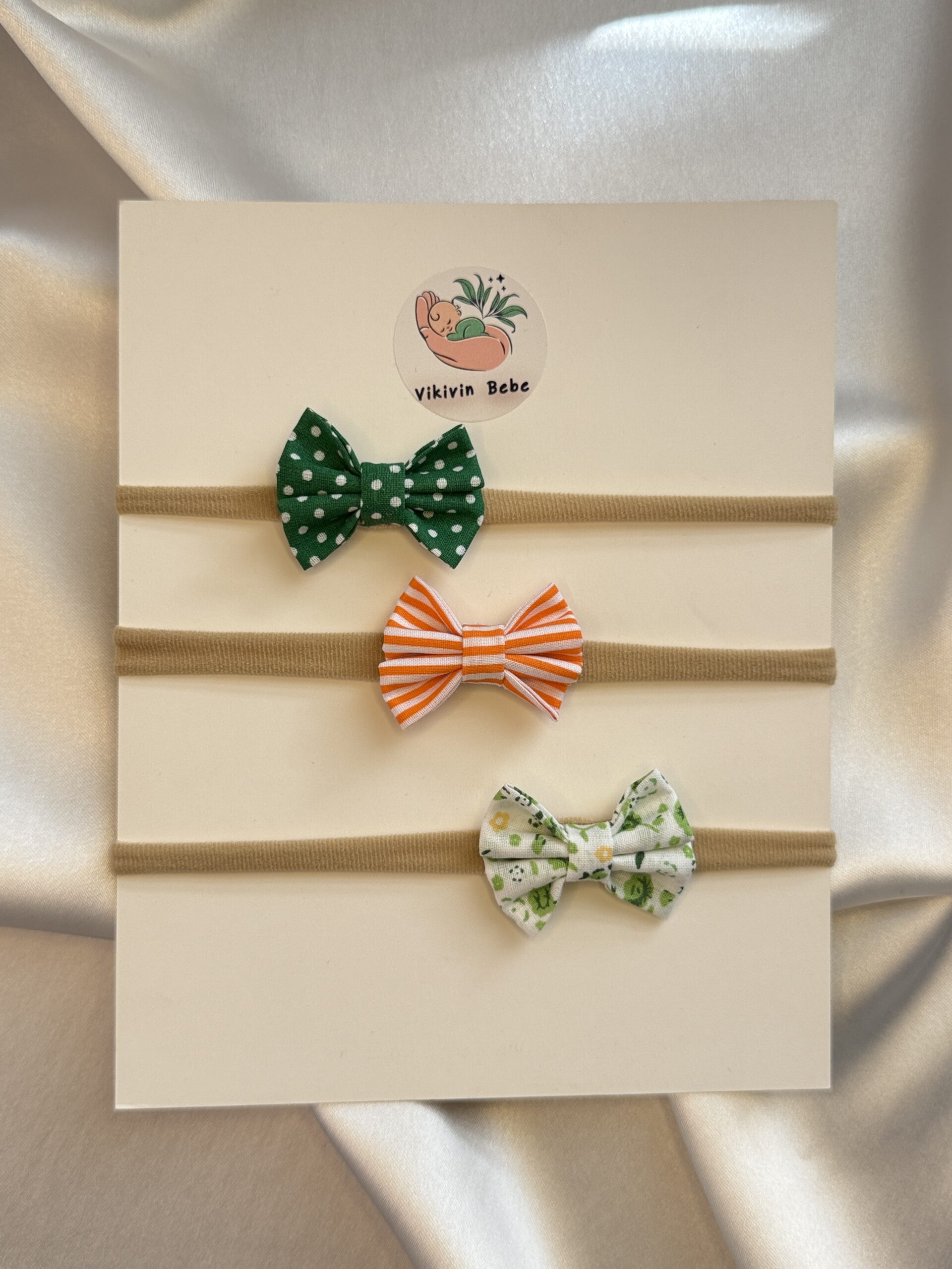 Bebek saç bandı 3’lü set – yeşil puantiyeli, turuncu puantiyeli ve yeşil çiçek desenli mini fiyonklar; yumuşak esnek nude bant, yenidoğan ve çocuklar için konforlu.